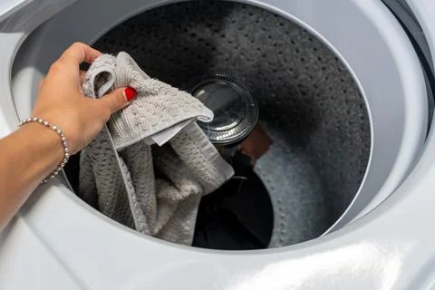 Hand loading dirty laundry into a large top-loading washing machine drum Stock Photos