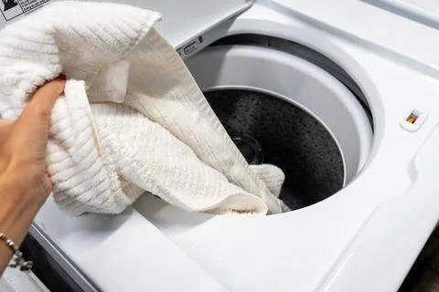 Hand loading laundry into a large top-loading washing machine Stock Photos