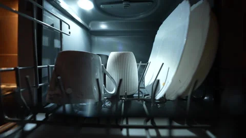 Hand loading mug and plates into modern dishwasher under warm kitchen lighting. Stock Footage 326059726