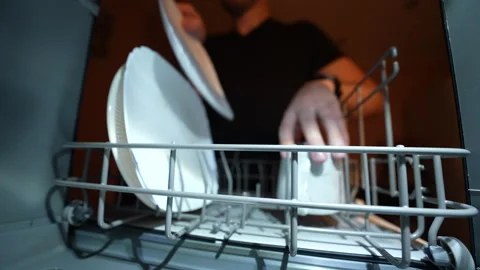 Hand loading mug and plates into modern dishwasher under warm kitchen lighting. Stock Footage 326059859