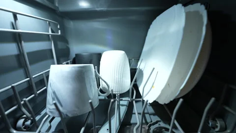 Hand loading mug and plates into modern dishwasher under warm kitchen lighting. Vídeos de archivo 326059860