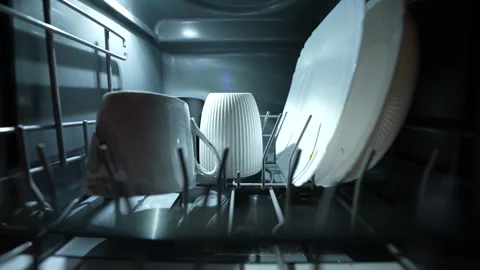 Hand loading mug and plates into modern dishwasher under warm kitchen lighting. Stock Footage 326059894
