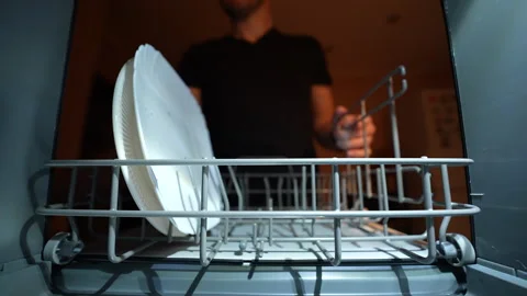 Hand loading mug and plates into modern dishwasher under warm kitchen lighting. Vídeos de archivo 326059895