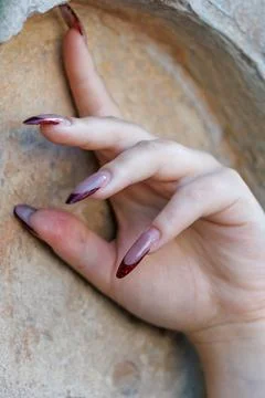 Hand with long, elegant nails resting on textured stone surface. Stock Photos
