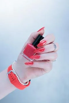 Hand with long nails and a bottle of bright red nail polish Stock Photos