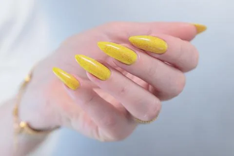Hand with long nails and a bright yellow orange nail polish Stock Photos