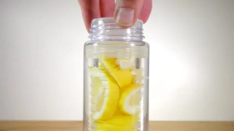 Hand lowering lemon slices into a fruit infuser water bottle. Stock-Footage 200875425