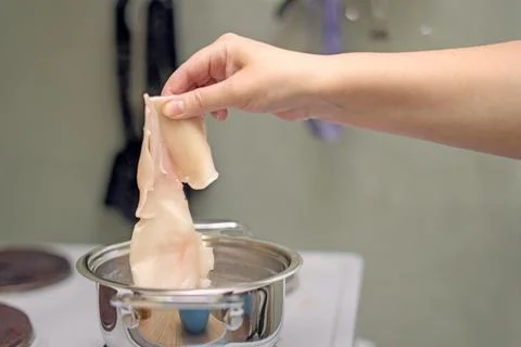 Hand lowering squid meat into boiling water in a pot for cooking seafood Stock Photos