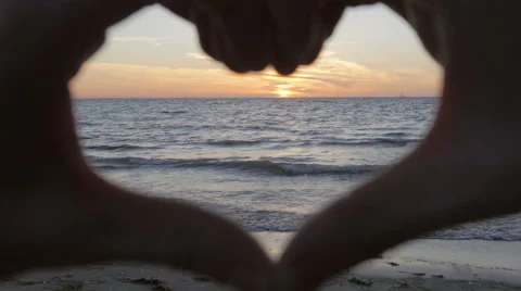 Hand made heard encompassing the sun down at the beach Stockbeeldmateriaal 51463298