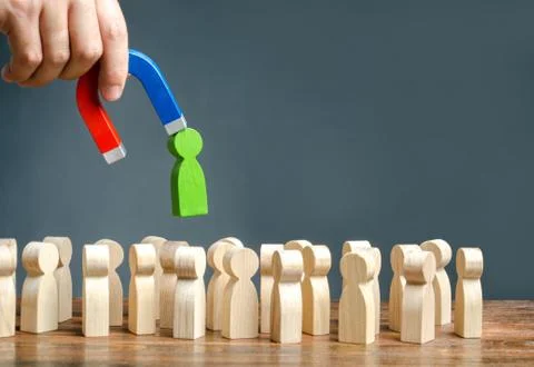 A hand with a magnet pulls green human figure out of the big crowd of people. Stock Photos