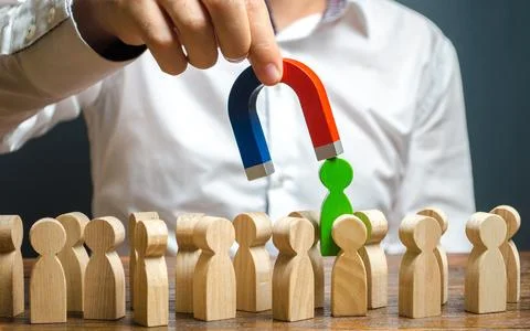 A hand with a magnet pulls green human figure out of the big crowd of peopl.. Stock Photos