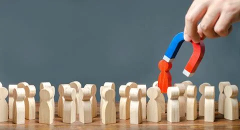 A hand with a magnet pulls a red human figure out of the crowd. Identify disl Stock Photos