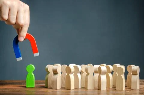 A hand with a magnet is trying to pull a green figure of a person out of a cr Stock Photos