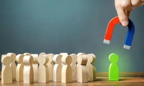 A hand with a magnet is trying to pull a green figure of a person out of a cr Stock Photos