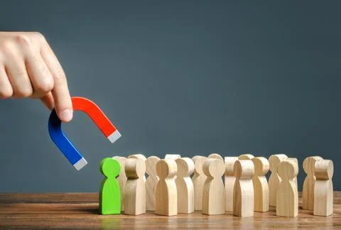 A hand with a magnet is trying to pull a green figure of a person out of a .. Stock Photos