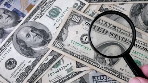 Hand with magnifying glass checking 100 USA dollar banknote on money backgr.. Видео 314394933