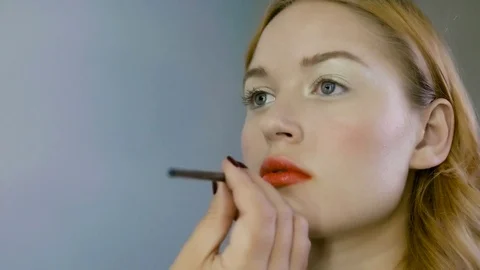 Hand of make-up master, painting lips of young beautiful model. Makeup in 스톡 동영상 82084198