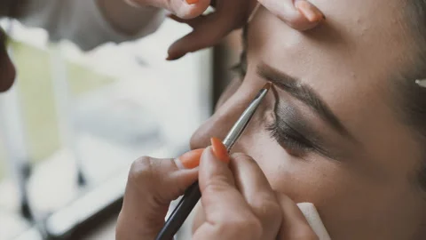 Hand of makeup artist makes makeup on the eyebrows of a beautiful young woman Stock Footage 154143083