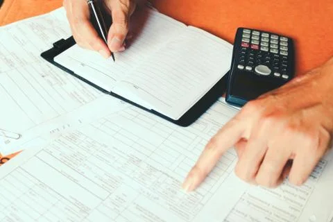 Hand making notes in a notebook with a pen and using counting calculator at.. Stock Photos
