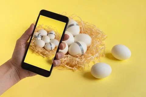 Hand making photo of white easter eggs in nest on illuminating yellow background Stock Photos