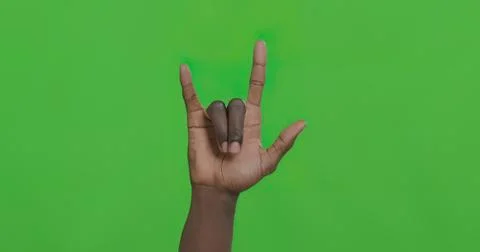 Hand making the rock and roll sign against green background Stock Photos