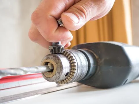 Hand of a man changing a drill of an electric drill on a wooden table. concep Stock Photos