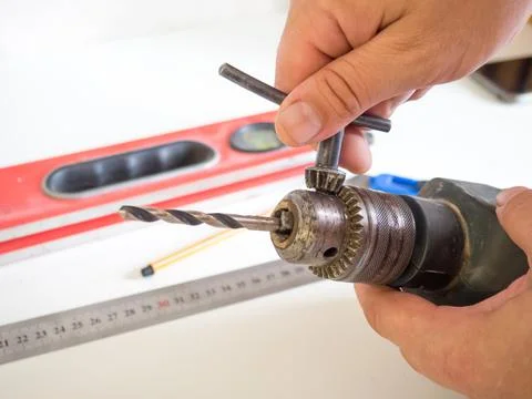 Hand of a man changing a drill of an electric drill on a wooden table. concep Stock Photos