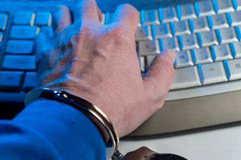 Hand of a man in handcuffs on a background of a computer keyboard Stock-Fotos