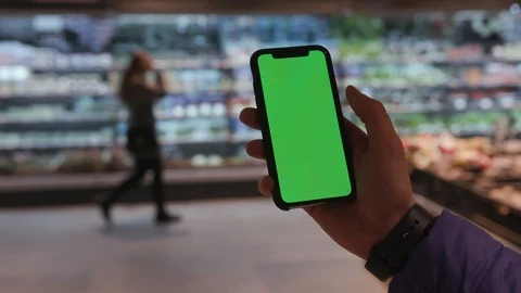 Hand of man holding black smartphone in hand with green screen in supermarket Video stock 106300935