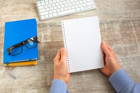 Hand of man holding an open notebook on wooden office desktop. Stock Photos