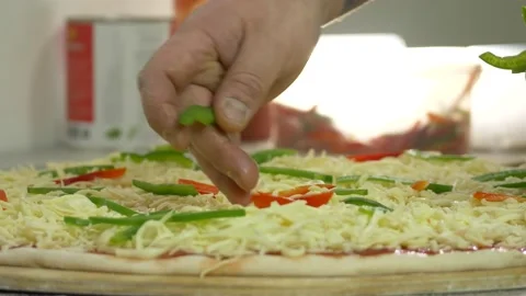 Hand of a man in a kitchen putting bell pepper on a pizza 4K Stock Footage 192453559