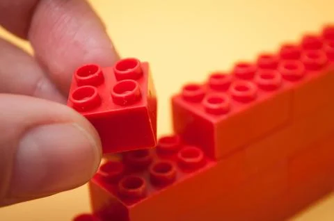 Hand of man playing with red plastic bricks construction Stock Photos