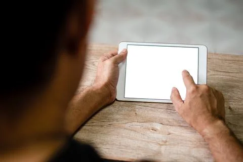 Hand of a man touching tablet device with a blank white screen on the desk .. Stock Photos