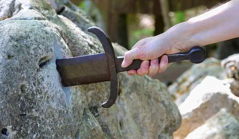 Hand of a man trying to pull the legendary Excalibur sword from a rock Fotos Stock