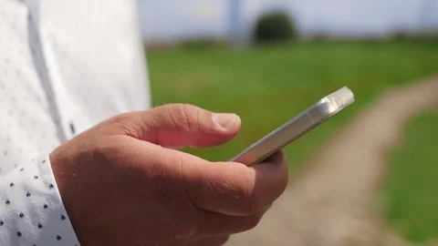 Hand of man using and scrolling phone in the background of a field. Close up Stock Footage 115133105