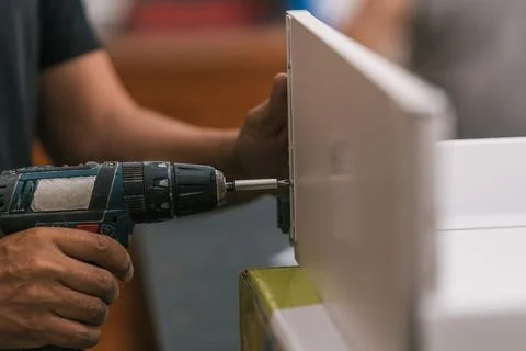 Hand of a man using a drill into a piece of furniture in a workshop. Stock Photos