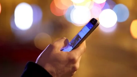 Hand of man using smartphone, city lights in background 库存影片 74721300