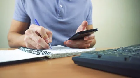 Hand of a man working at computer and using smartphone and writing in notebook Stock Footage 83378736