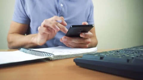 Hand of a man working at computer and using smartphone and writing in notebook Stock Footage 83781476