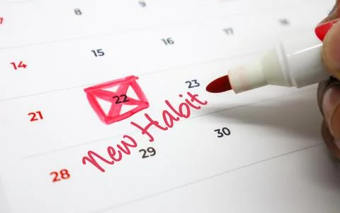 Hand marks a calendar date with a red pen, signaling the start of a new hab.. Stock Photos