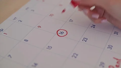 A hand marks the date on a calendar with a red marker, indicating an important Stockbeeldmateriaal 337556521