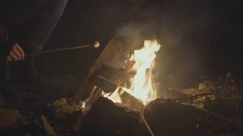 Hand with marshmallow on a stick being roasted over a camping fire at night Stock Footage 130067846