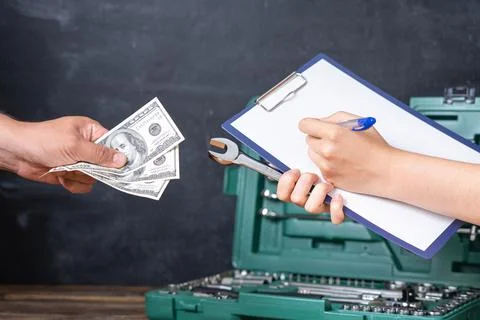Hand of a master mechanic with a tablet for notes and a man's hand with dolla Stock Photos