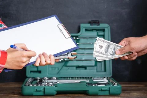 Hand of a master mechanic with a tablet for notes and a man's hand with dolla Stock Photos