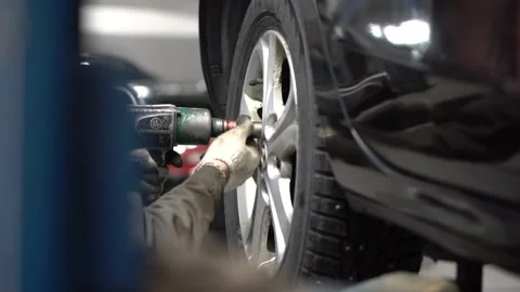Hand of a master using tool unscrews bolts from wheel cap of sedan lifted up Stock Footage 155965741