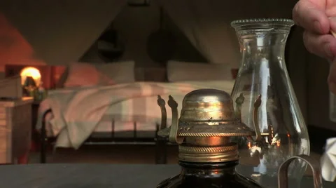 Hand with match lighting old fashioned oil lamp with safari tent in background Stock Footage 46374157