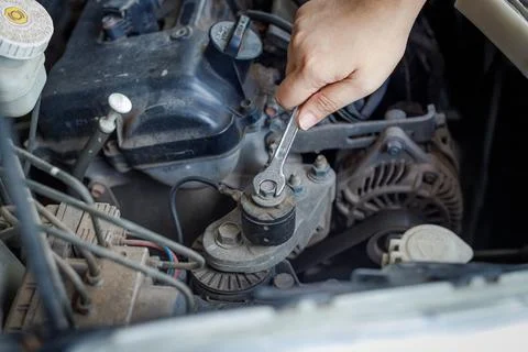 Hand of mechanic using a silver combination wrench to work on a pulley bolt Stock Photos