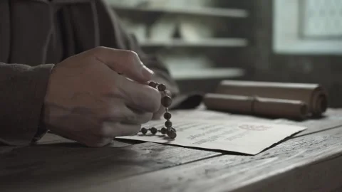 Hand of a medieval monk holding and counting rosary beads at a table Stock Footage 338991332