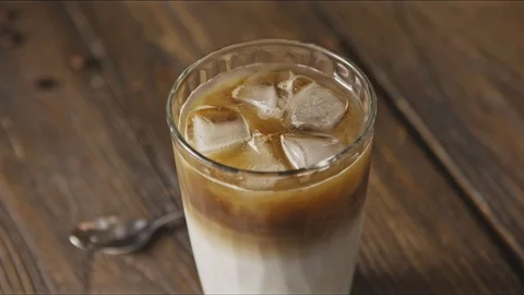 Hand mixes fresh cold coffee drink with spoon on a wooden background. Stock Footage 129637822
