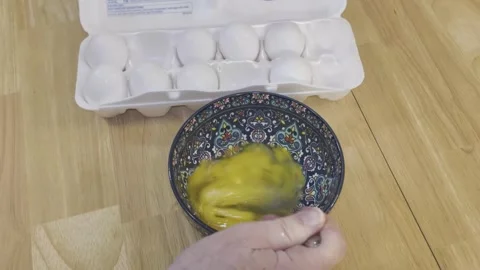 Hand mixes scrambles eggs with a fork in patterned bowl Stock Footage 340112189